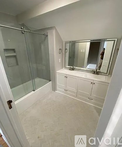 A bathroom with a glass shower door and a vanity with a mirror above it.