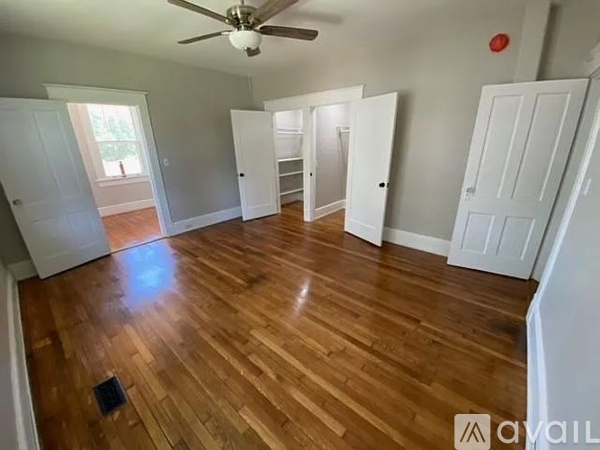A room with wooden floors and white walls, featuring a ceiling fan and a few doors.