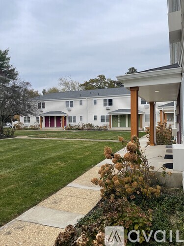 A white house with a red door is surrounded by a green lawn.