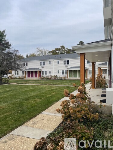 A white house with a red door is surrounded by a green lawn.