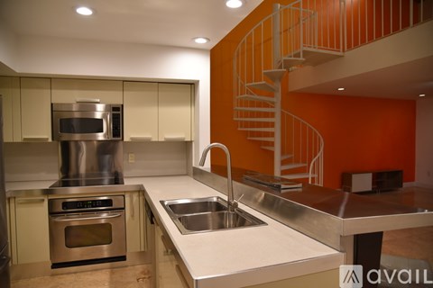 A modern kitchen with a stainless steel sink and a spiral staircase.