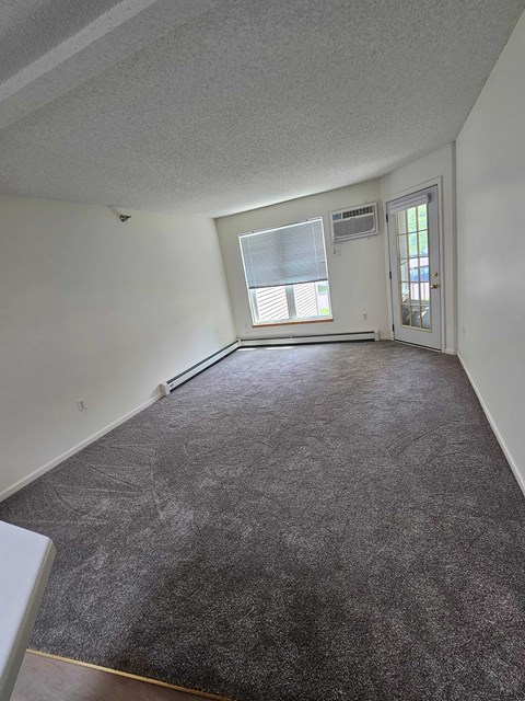 A room with a carpeted floor and a window with blinds.