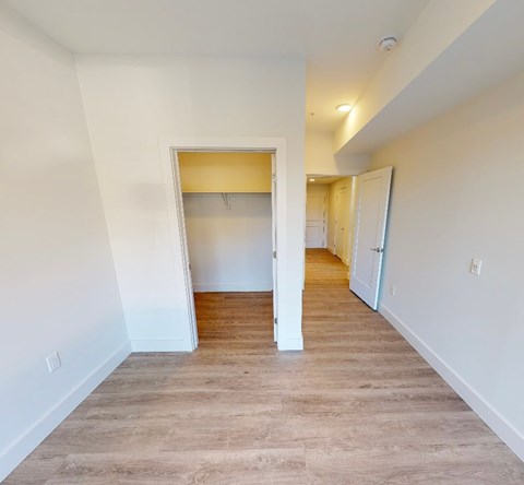 A room with a white wall and a wooden floor with a doorway leading to another room.