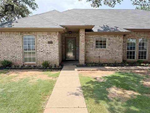 A house with a brown roof and a brick exterior has a white door and windows.