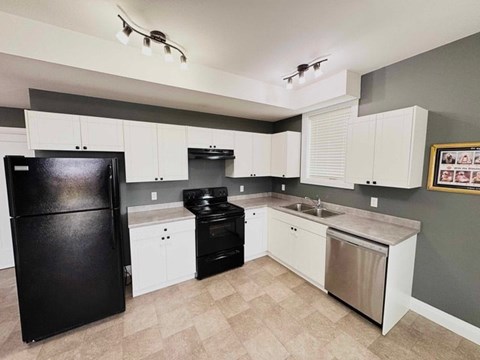 A black refrigerator sits in a kitchen with white cabinets and a black stove.