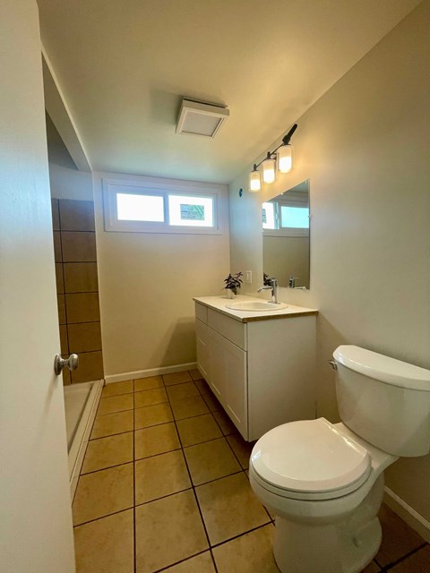 A white toilet in a small bathroom with a white cabinet and a mirror above it.
