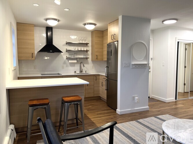A modern kitchen with a white countertop and dark bar stools.