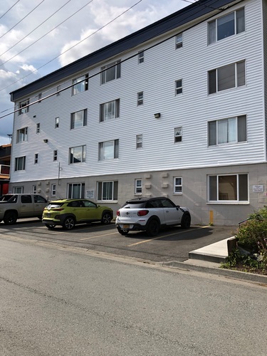 A white building with a green car and a white car parked in front.