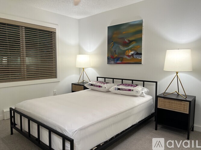 A bedroom with a bed, two lamps, and a painting on the wall.