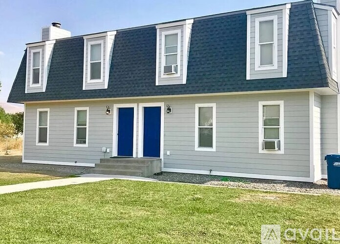 A house with a blue door and a grey facade is for sale.