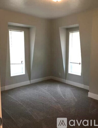A room with grey carpet and two windows.