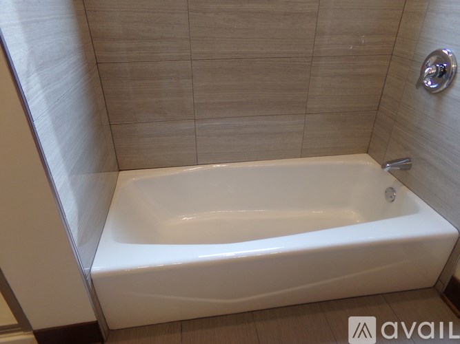 A white bathtub in a bathroom with beige tiles.
