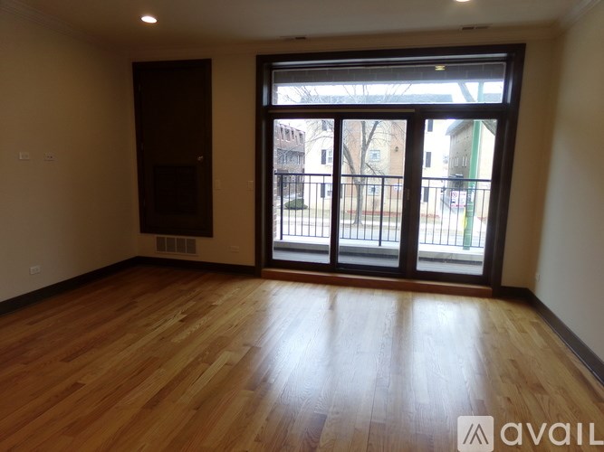 A room with wooden flooring and a large window with a view of a fence and buildings outside.