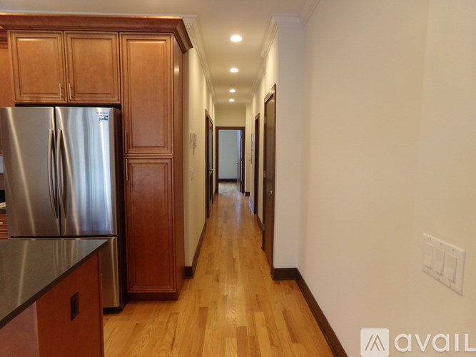 A long hallway with wooden floors and a refrigerator on the left side.