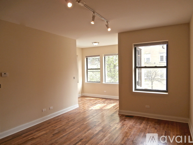 A spacious room with wooden floors and two windows.