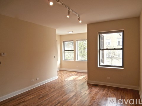 A spacious room with wooden floors and two windows.