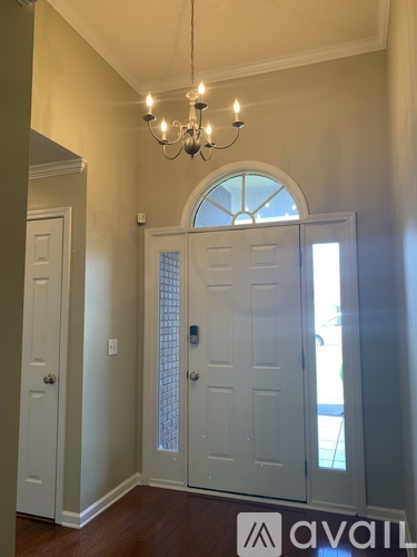 A chandelier hangs over a white door in a room with wooden floors.