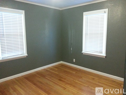 A room with wooden floors and two windows with blinds.