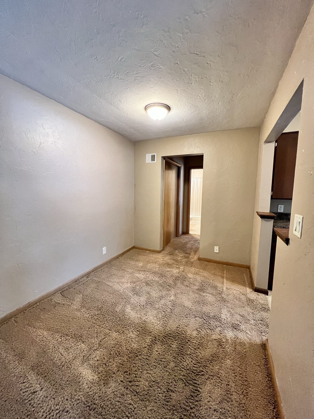 an empty living room with carpet and a door to a hallway