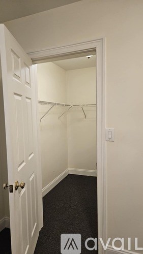 A white door with a gold handle is open to a hallway with a black carpet.
