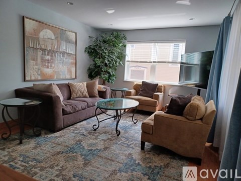 A living room with a brown couch, a glass table, and a painting on the wall.