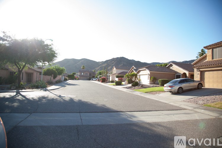 A sunny day in a quiet residential street with houses on both sides and a car parked on the right.