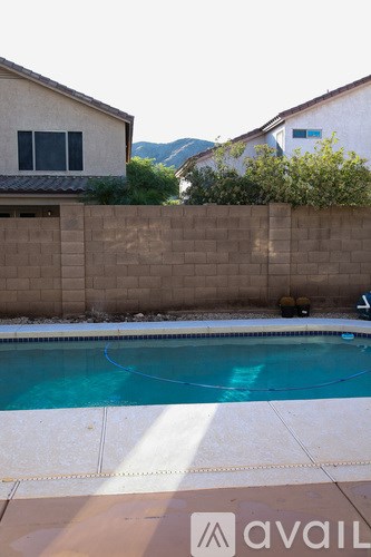 A pool in a backyard with a tan wall and a house in the background.