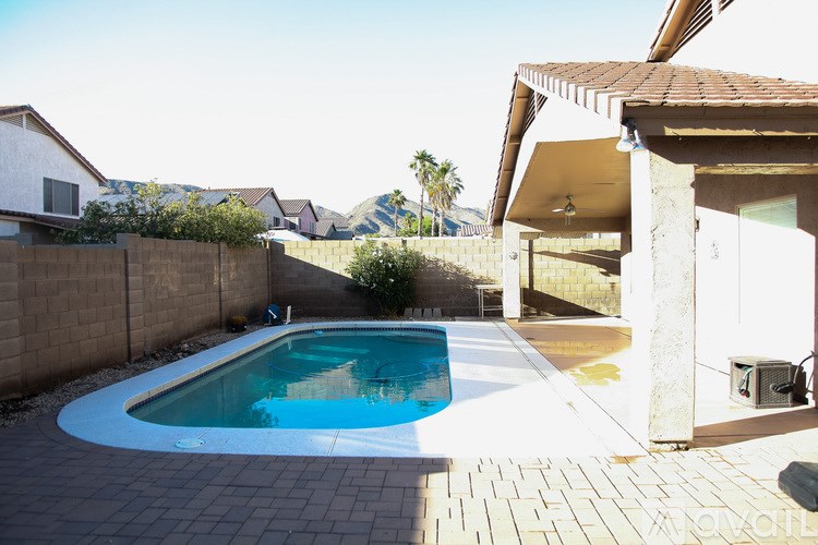 A small pool in a backyard with a patio and a house in the background.