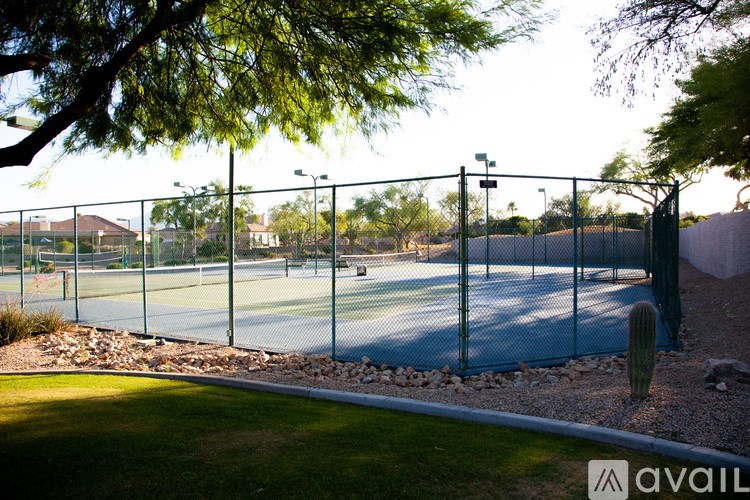 Tennis court surrounded by a fence with trees in the background.