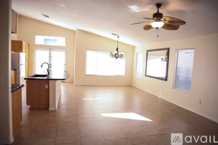 A spacious living room with a kitchen area to the left and a ceiling fan above.