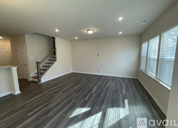 A spacious room with wooden flooring and a staircase in the background.
