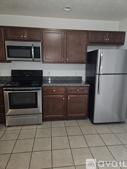 A kitchen with a black stove top oven, a black microwave, a silver refrigerator, and brown cabinets.