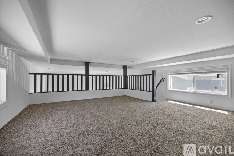 A spacious room with a carpeted floor and a staircase with black railings.