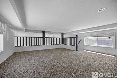 A spacious room with a carpeted floor and a staircase with black railings.