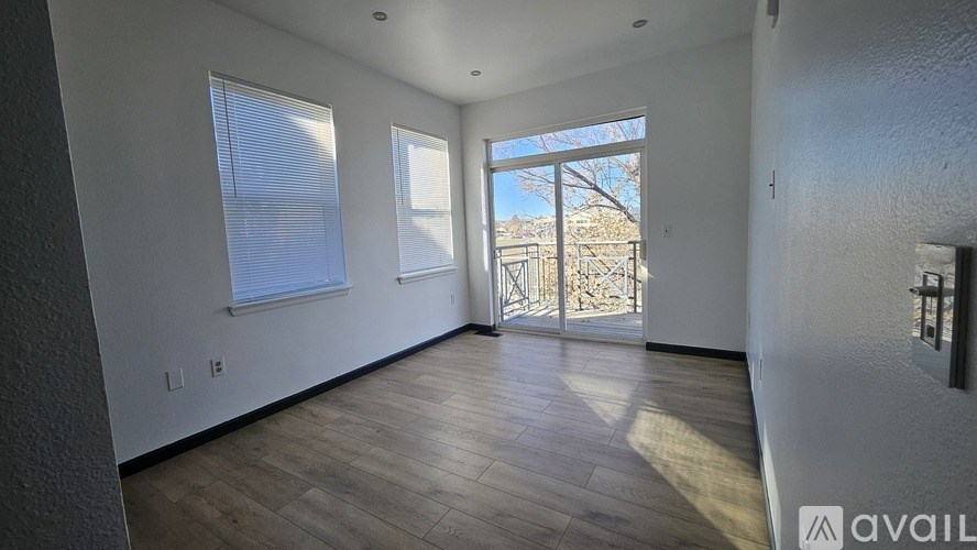 A spacious room with wooden flooring and a view of a balcony through the door.
