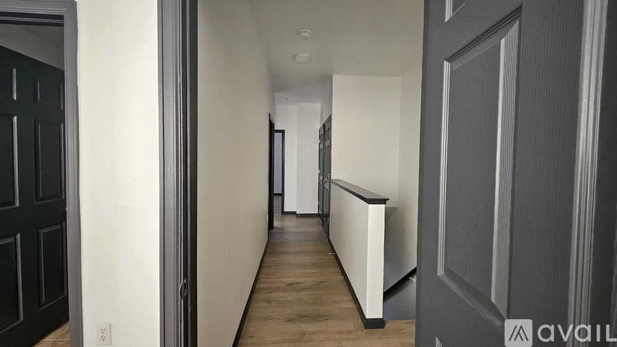 A long hallway with a white wall and a black door on the left.