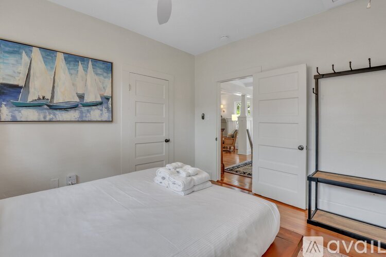 A bedroom with a white bed and a painting of sailboats on the wall.