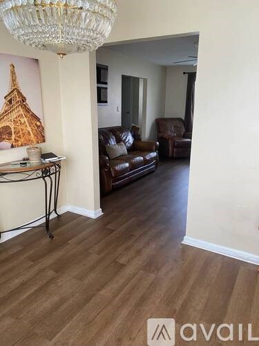A living room with a chandelier, a couch, and a painting of the Eiffel Tower.