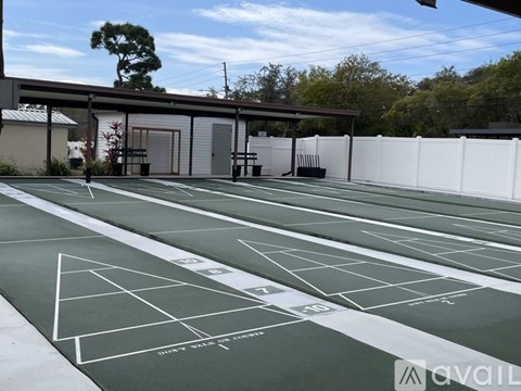 A tennis court with green surface and white lines, surrounded by a white fence and a building in the background.