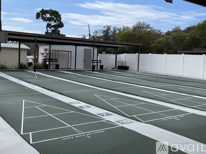 A tennis court with green surface and white lines, surrounded by a white fence and a building in the background.