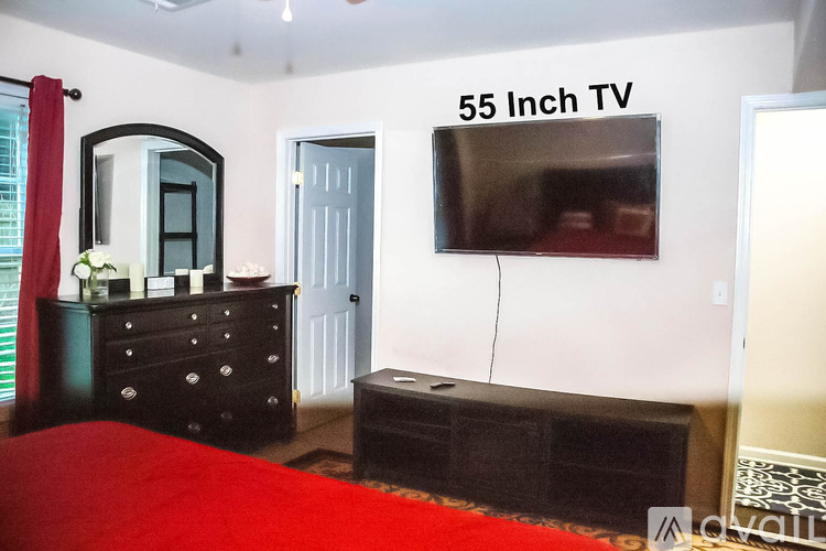 A bedroom with a red bedspread and a 55 inch TV mounted on the wall.