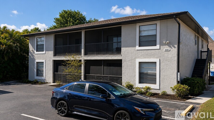A blue car is parked in front of a two-story apartment building.