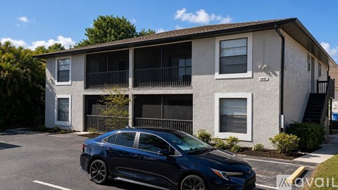 A blue car is parked in front of a two-story apartment building.