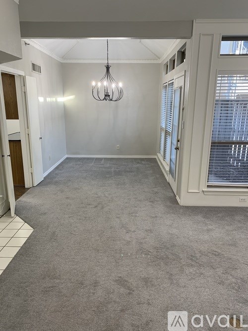 A spacious room with a grey carpet and a chandelier hanging from the ceiling.