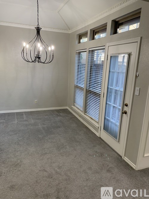 A room with a grey carpet, a chandelier, and a door with blinds.