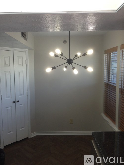 A chandelier with eight lights hangs from the ceiling in a room with white walls and a wooden floor.