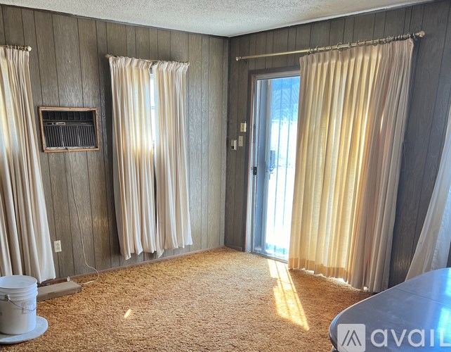 A room with a carpet, a bucket, and curtains.
