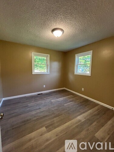 A room with wooden flooring and two windows.