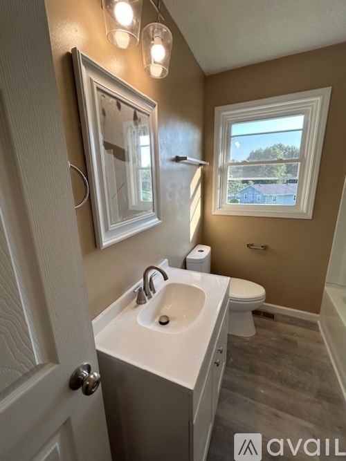 A bathroom with a toilet, sink, mirror, and light fixture.
