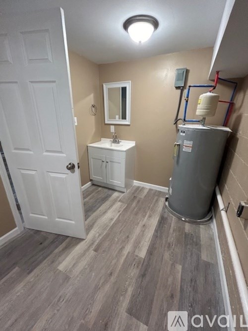 A bathroom with a white door, a mirror, a sink, and a trash can.
